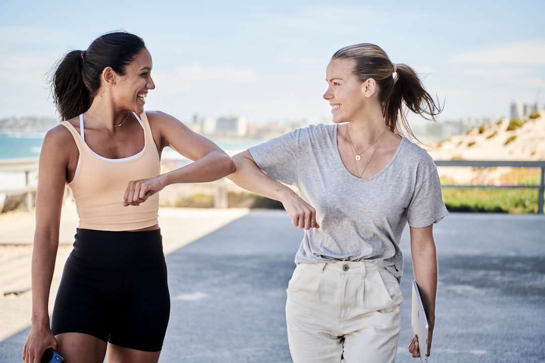 woman-in-gray-shirt-elbow-bumping-with-woman-in-sports-outfit-orcayrmulxw